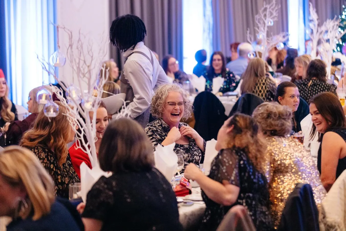 A bunch of friends all laughing at their table at a Christmas party
