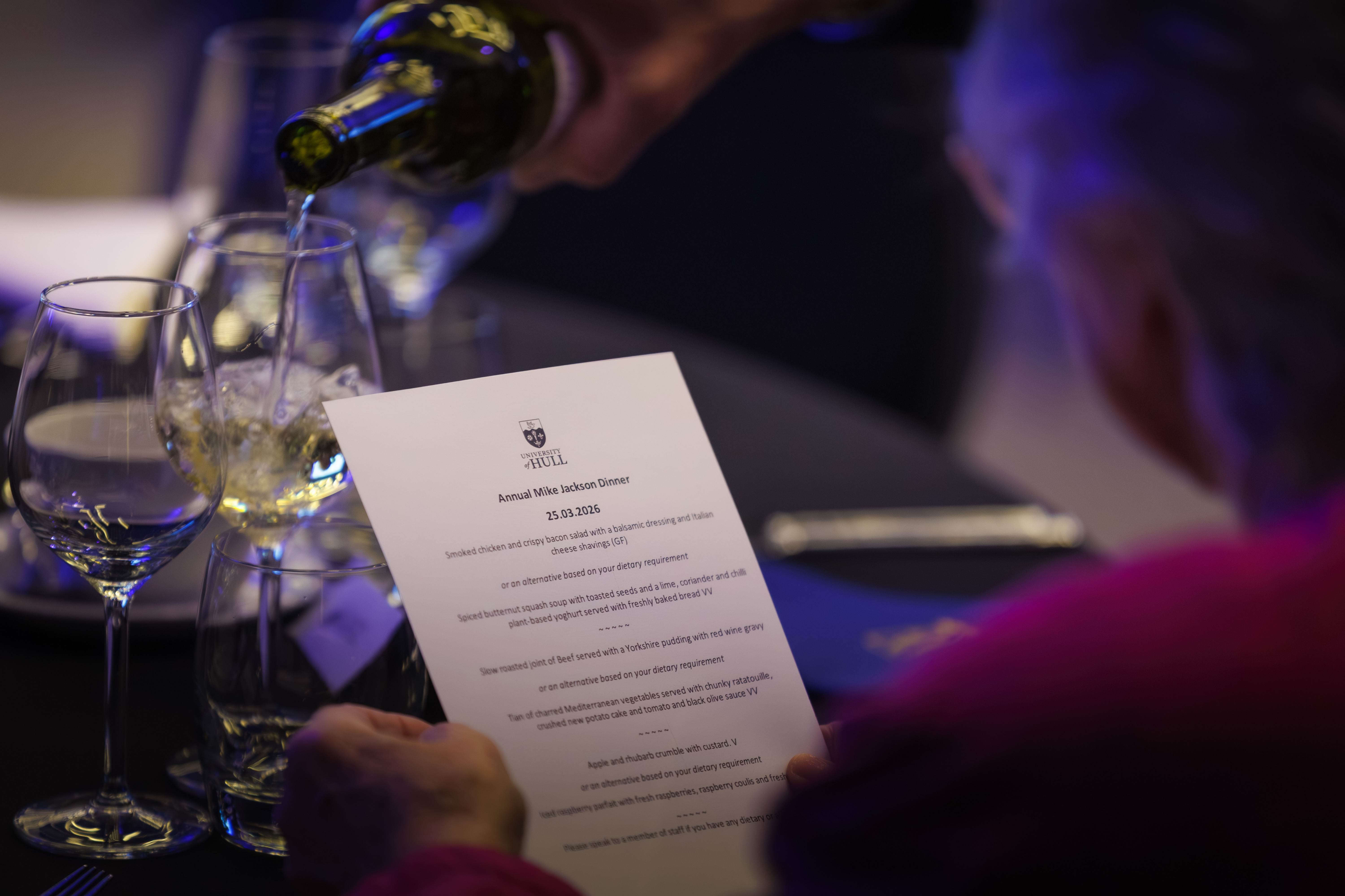 A woman examines a menu while wine is poured into her glass