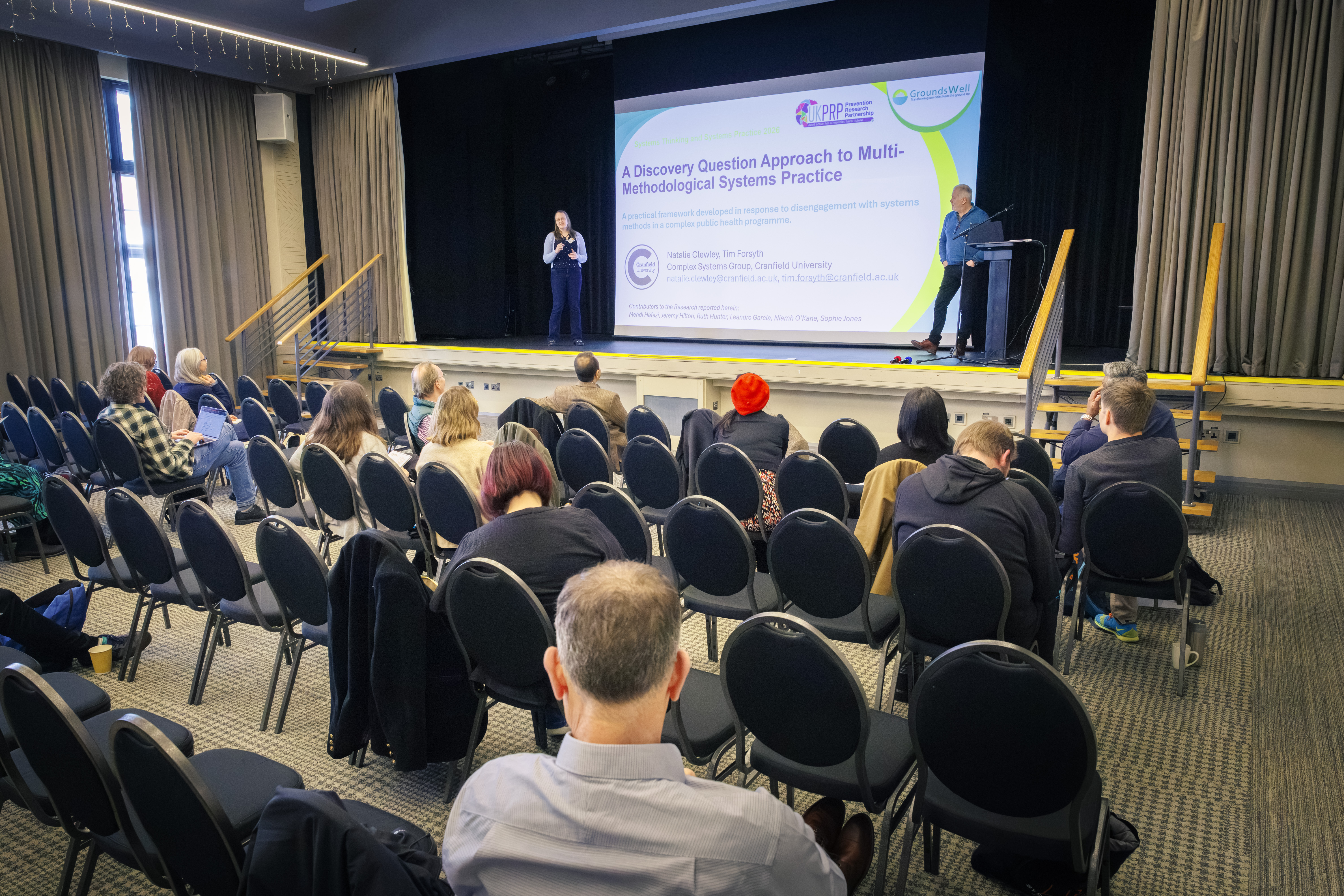 A handful of people watch a presentation in a large conference room that's partitioned in half