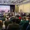 A large group of people watch a panel discussion in a bright, modern room
