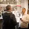 Two people stand talking with a drink in a bar