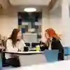 Two women sit chatting at a table over coffees