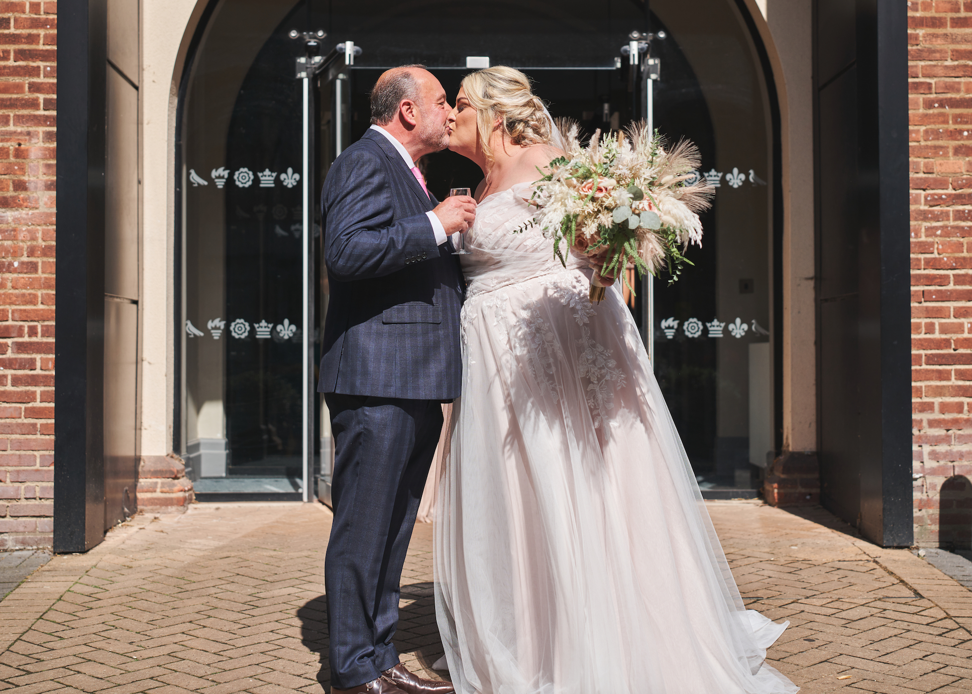 Bride and groom sharing a kiss outside their wedding venue, celebrating with champagne in the sunshine.