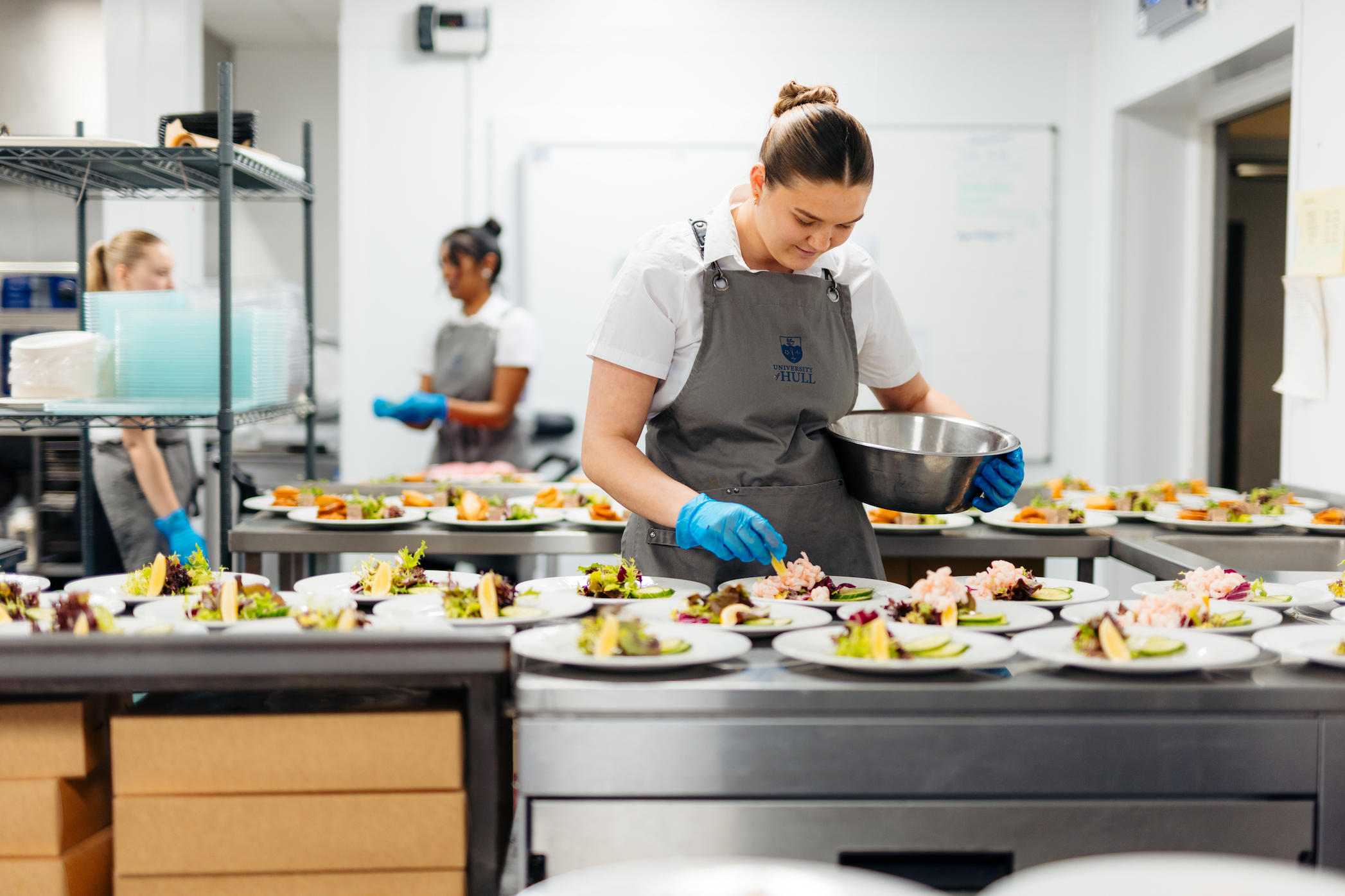 A female catering assistant puts the finishing touch on a plate, with a row of other finished plates