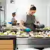 A female catering assistant puts the finishing touch on a plate, with a row of other finished plates