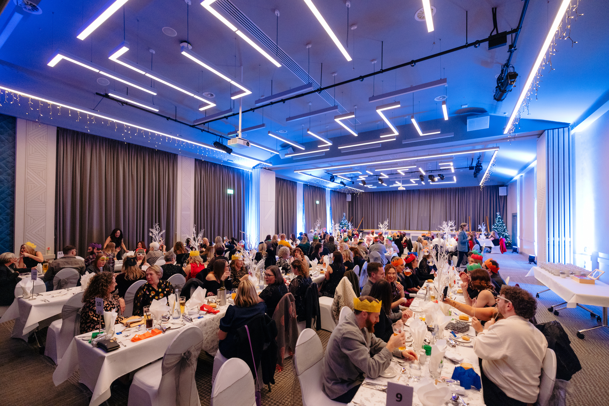 Large numbers of people wearing party hats sit at long tables in the Kingsley Suite