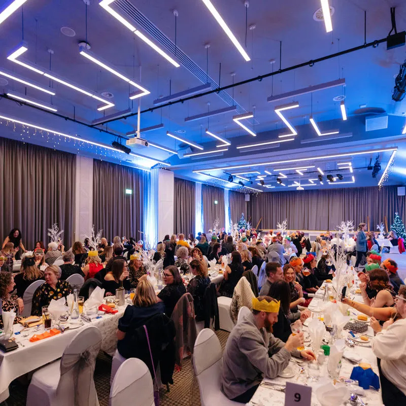 Large numbers of people wearing party hats sit at long tables in the Kingsley Suite
