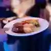 A waiter holding a white plate with beef, roast potatoes, carrots, sprouts and gravy on.