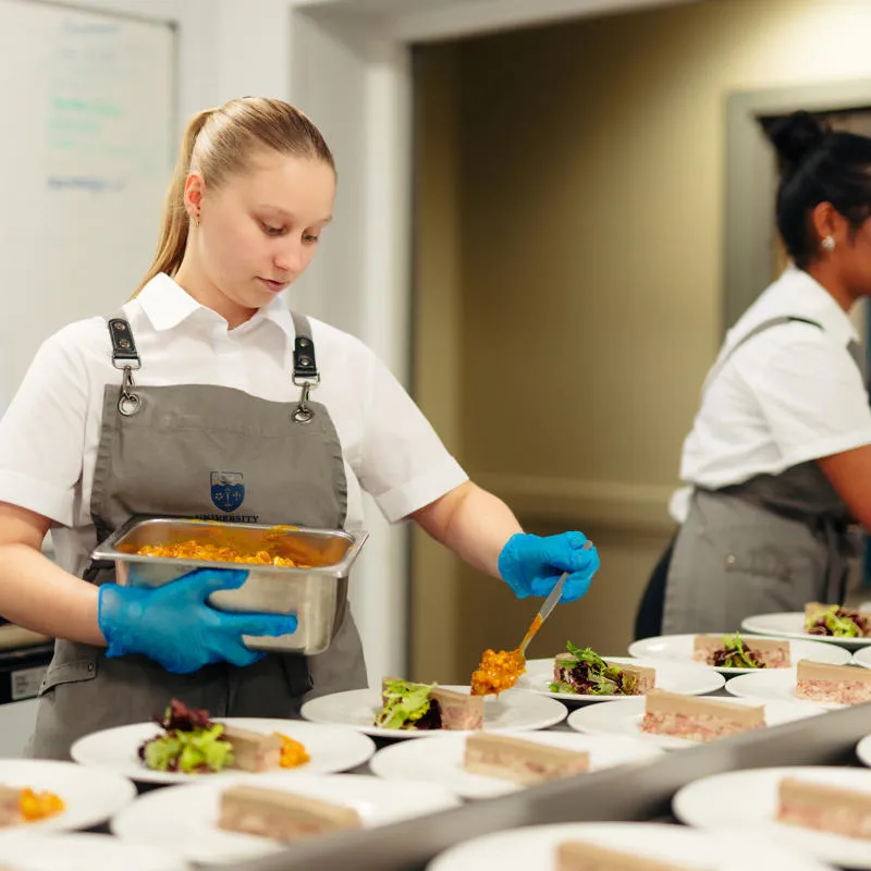A female catering assistant plates up part of a meal