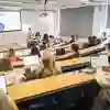Students sit in rows in a banked lecture theatre