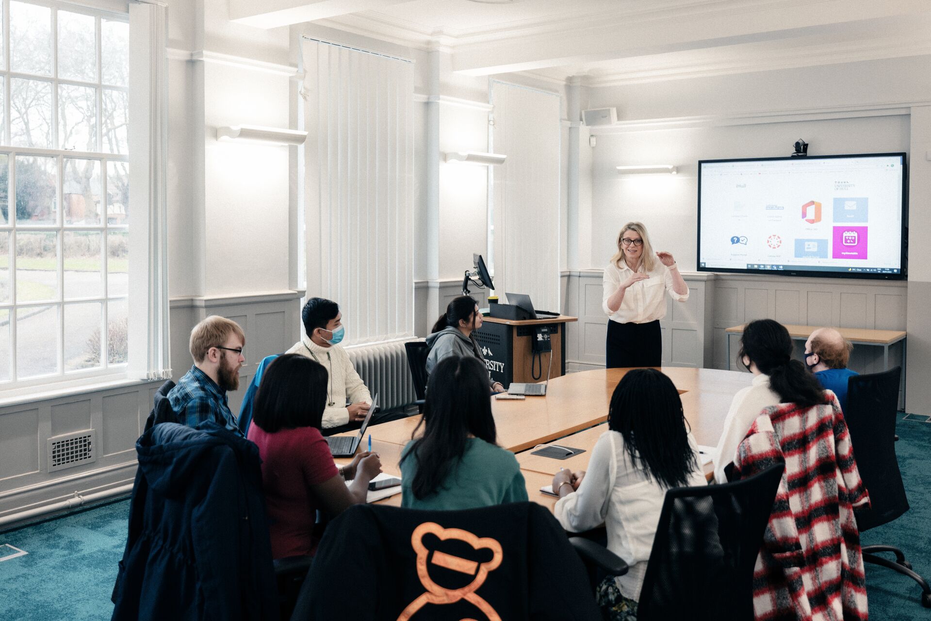 A woman gives a presentation to a small group of students in an executive boardroom